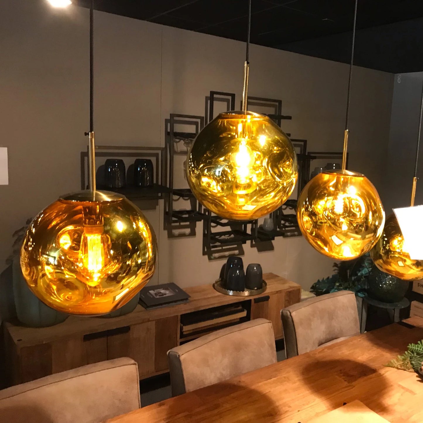 Three gold pendant lights hanging above a wooden table in a room with chairs and decor.
