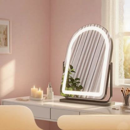 An arched LED vanity mirror with a built-in light stand, displayed on a white makeup desk in a softly lit pink room.
