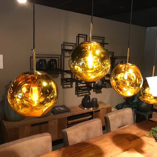 Three gold pendant lights hanging above a wooden table in a room with chairs and decor.