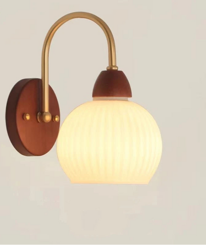 Wall-mounted light fixture with wooden base and gold arm on a plain background